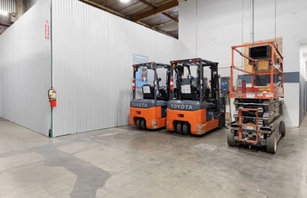 Two forklifts in a warehouse with a man on the lift.